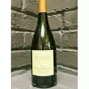 A bottle of Favalora Chardonnay 2018 displayed on a brick wall.