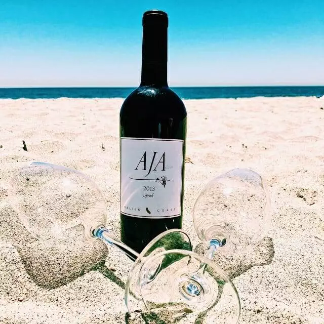 A bottle of wine and two glasses on the beach.