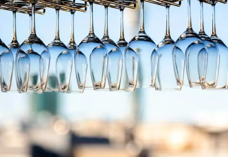 A row of wine glasses on a bar with a view of the city.