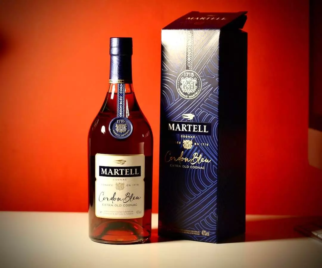 A bottle of martell on a table next to a box.