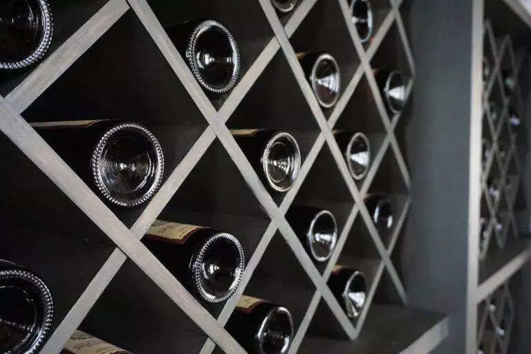 Custom wine racks provide a storage solution for wine collectors, elegantly showcasing a row of wine bottles in a wooden rack.