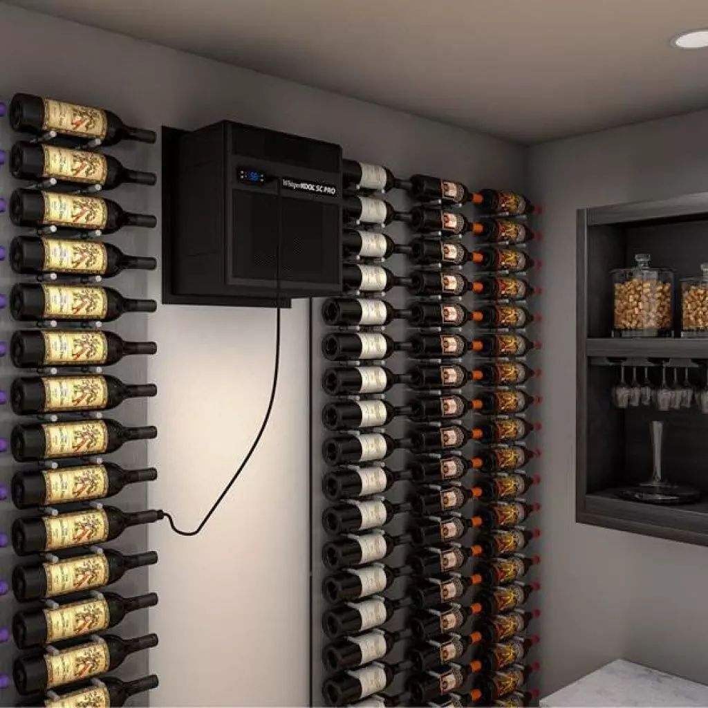A small wine cellar with wine bottles neatly stored on wall-mounted racks and a compact cooling unit on the wall. To the right, there is a shelf with glasses and jars of nuts.