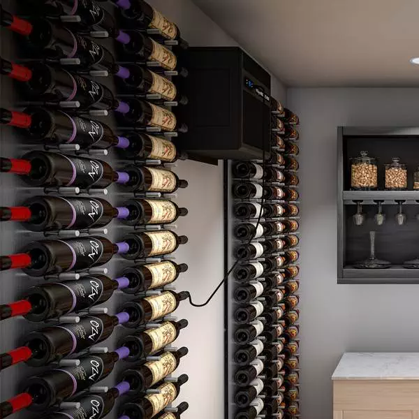 A small wine cellar featuring several racks of wine bottles along the walls, a cooling unit mounted on one wall, and a shelf with wine glasses and containers on the right.