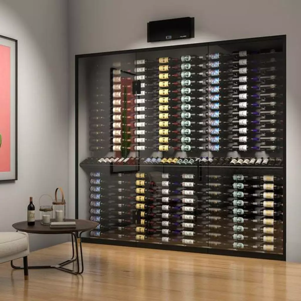 A glass-front wine storage unit filled with bottles is installed against a wall next to a lounge area with a small table holding two wine glasses, a wine bottle, and a corkscrew.