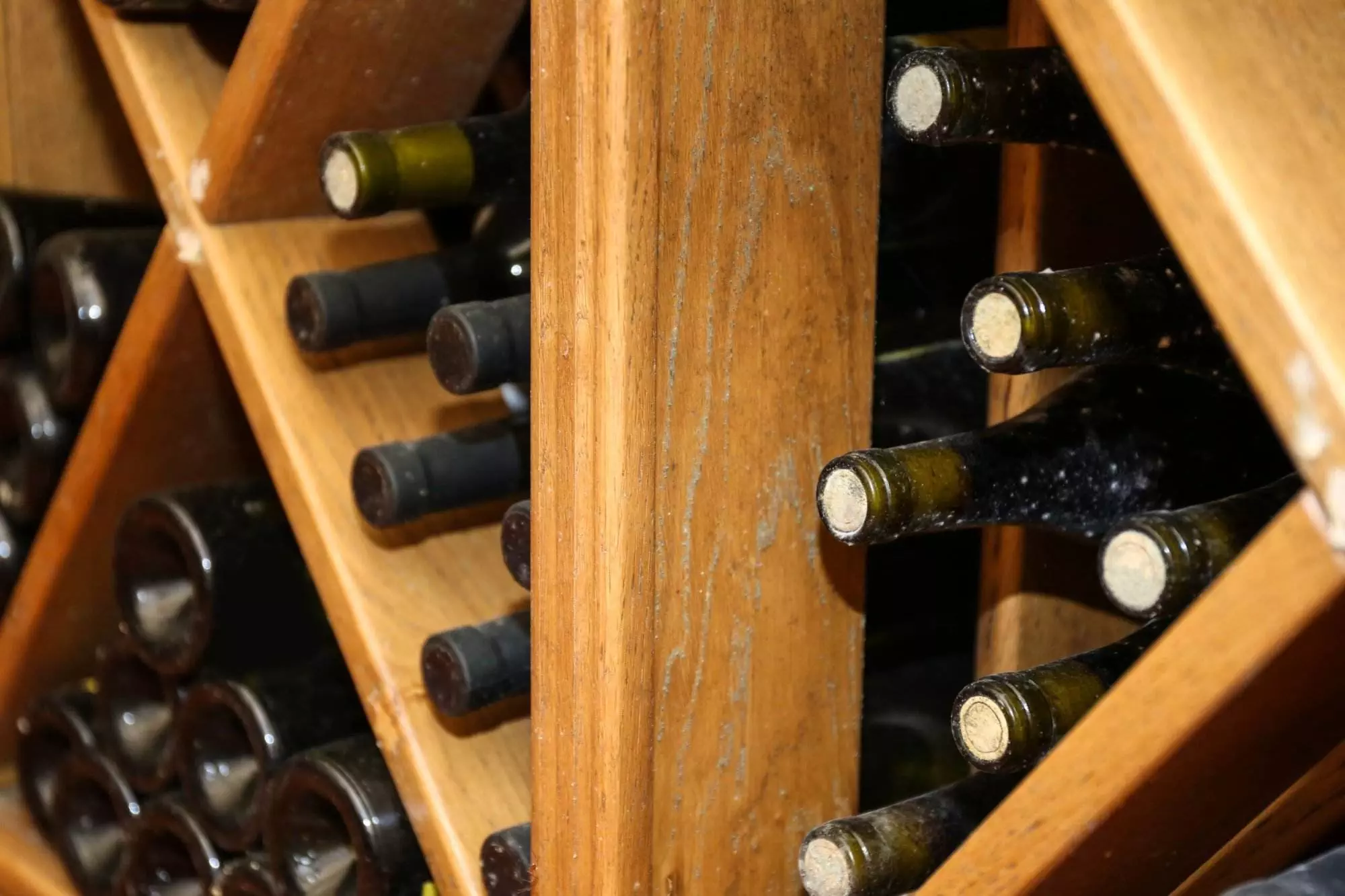 Dusty wine bottles stacked horizontally in a custom wine cellar, highlighting the age and storage of the collection.