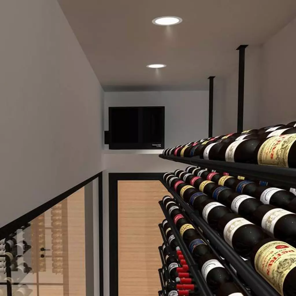 A narrow wine cellar with racks of wine bottles, white walls, wooden flooring, and a small black television mounted on the back wall.