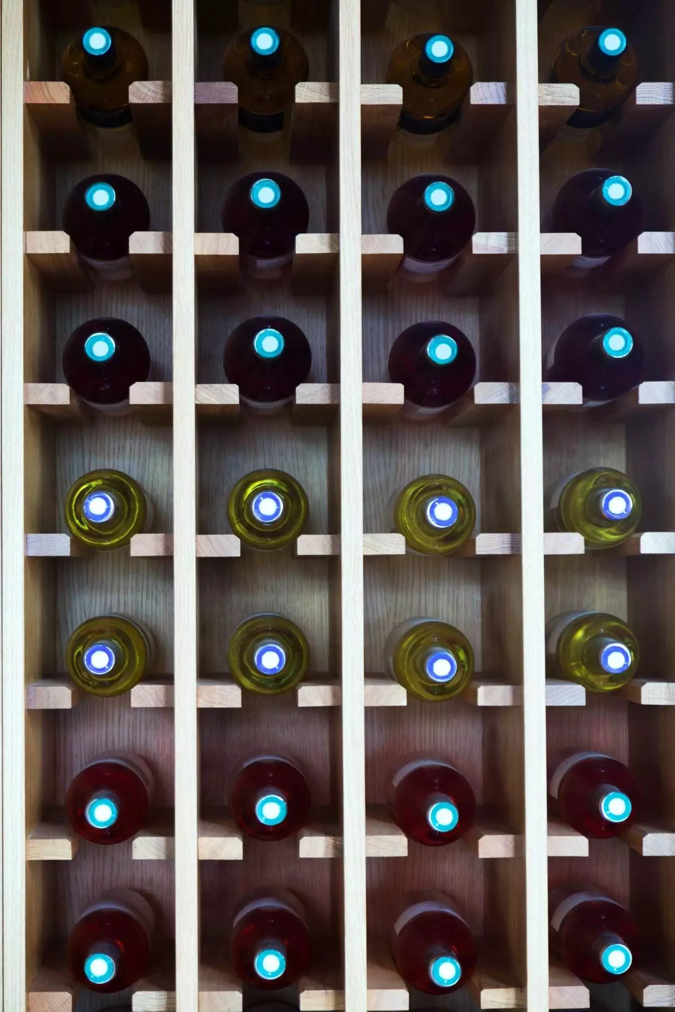 A wooden wine rack holding rows of bottles with dark and light labels, viewed from the bottom, showcasing the circular seals and Wine Hardware.