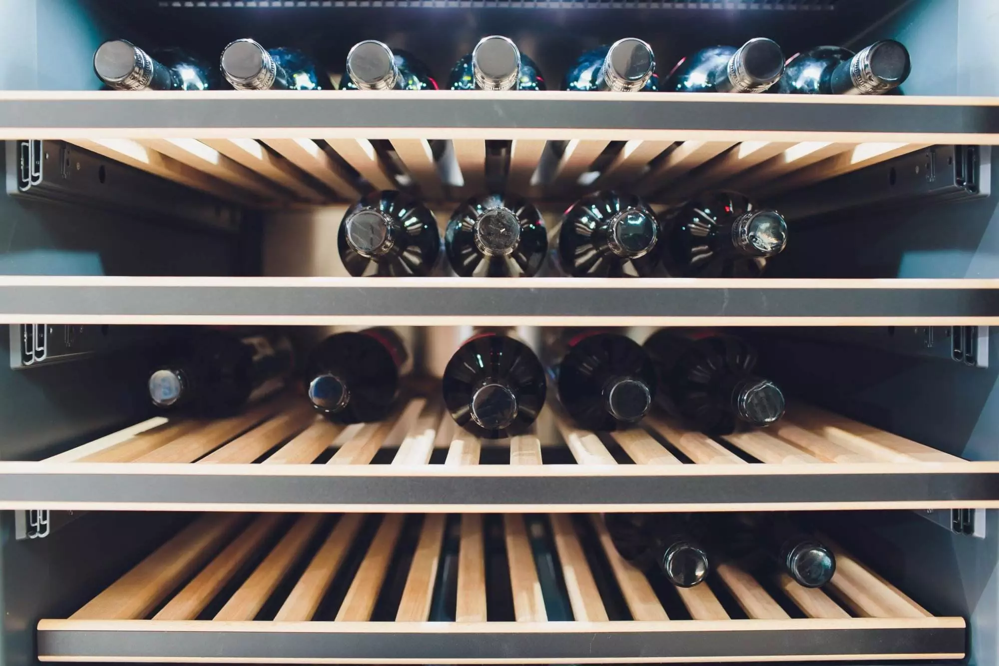 Wooden custom wine rack filled with various wine bottles in a modern refrigerator.