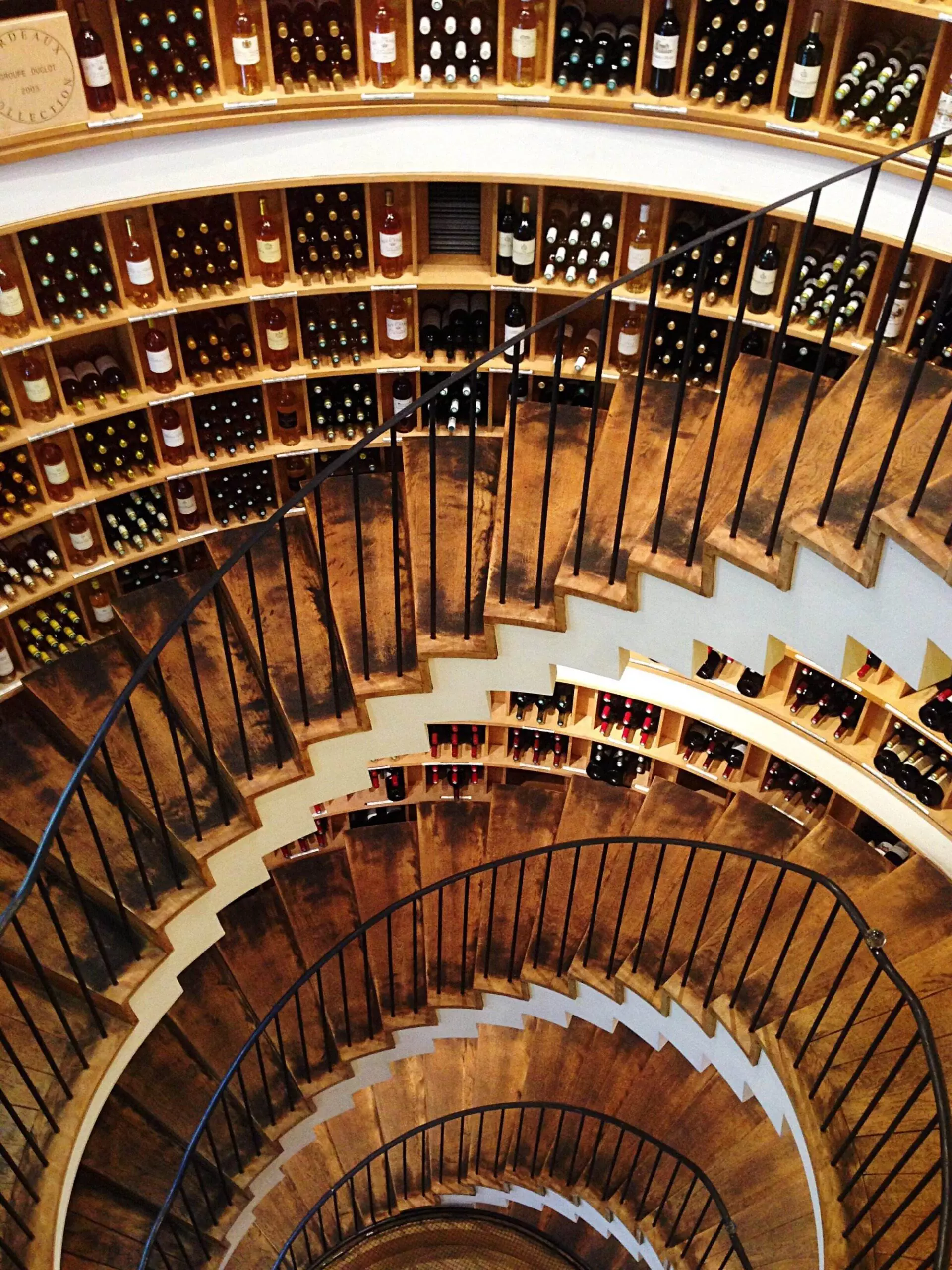 Spiral staircase encircled by shelves of wine bottles in a compact wine cellar offers an innovative storage solution for small spaces.