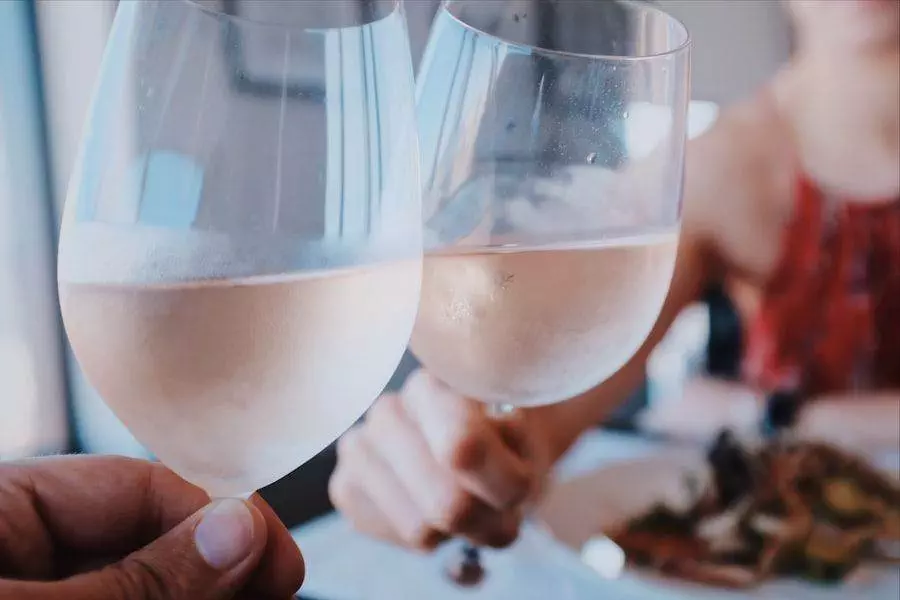 Two people clinking glasses of white wine over a table with plates of food in a casual dining setting.