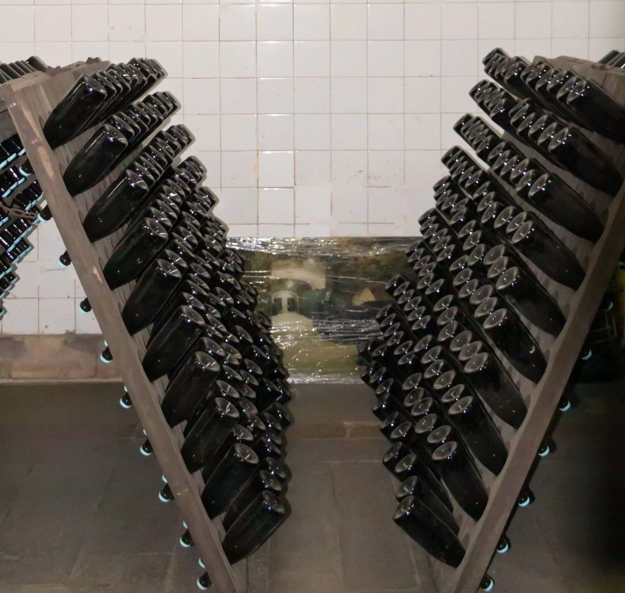 In a Napa Wine Cellar, sleek racks hold two sets of wine bottles angled downward in a V formation against white tile walls, ensuring optimal insulation for preserving quality.