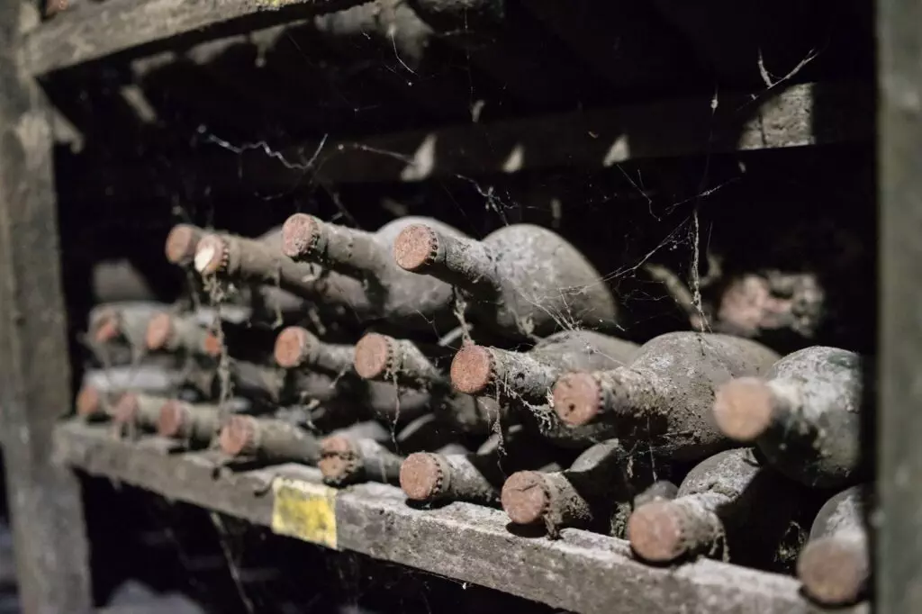 In the dimly lit cellar, old wine bottles, covered in dust and cobwebs, are expertly stacked horizontally on wooden racks. This Bay Area haven is meticulously designed for optimal wine storage while incorporating earthquake-proofing measures for safety and peace of mind.