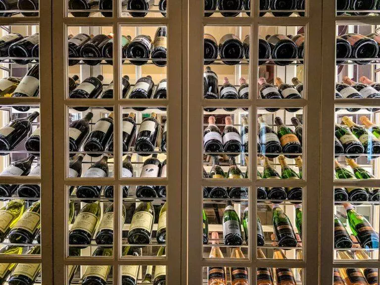 A wine cabinet filled with various bottles organized on angled shelves, viewed through a glass-paneled door.