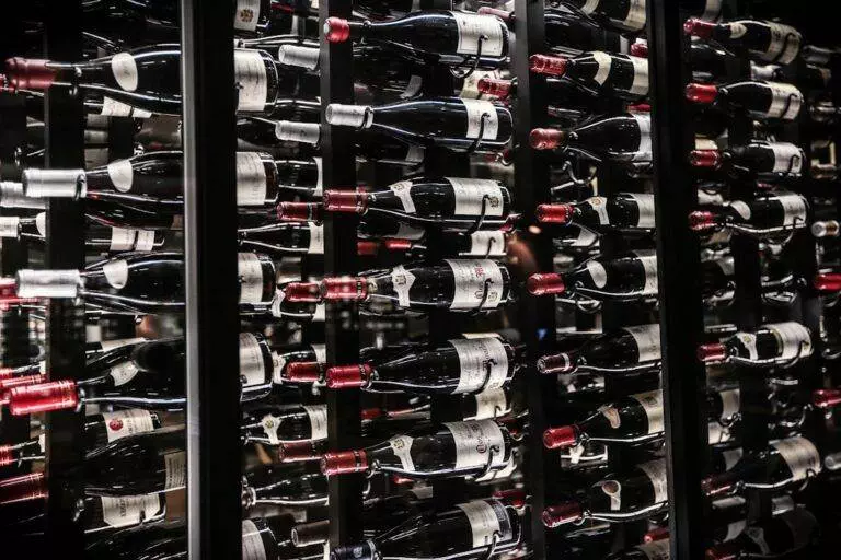 Bottles of wine stored horizontally on multiple racks in a dimly lit cellar, with a mix of red and white wine labels visible.