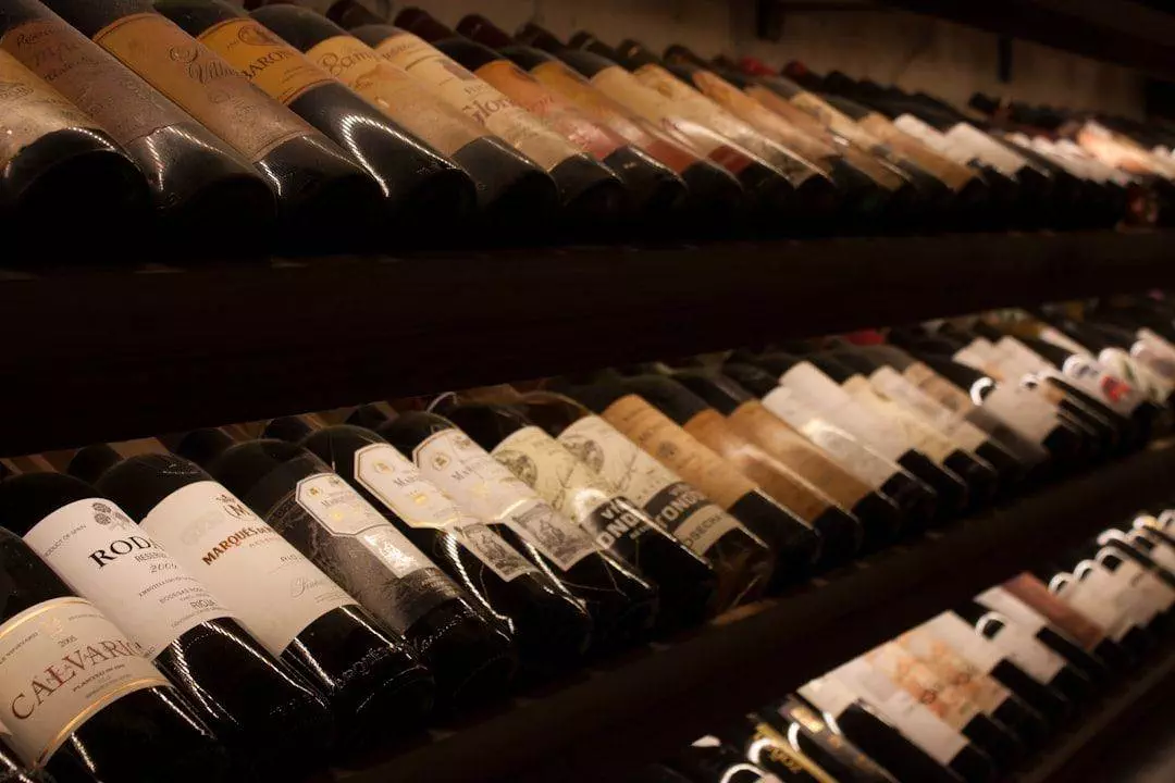 Rows of wine bottles are stored horizontally on shelves in a dimly lit cellar.