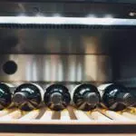 Five wine bottles are lying horizontally on a wooden rack inside a Danville wine cooler, a testament to quality wine refrigerators.