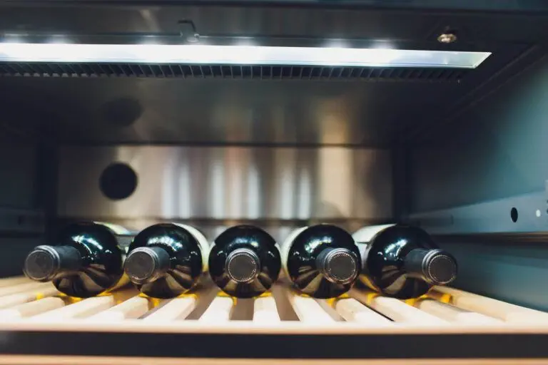 Five wine bottles are lying horizontally on a wooden rack inside a Danville wine cooler, a testament to quality wine refrigerators.